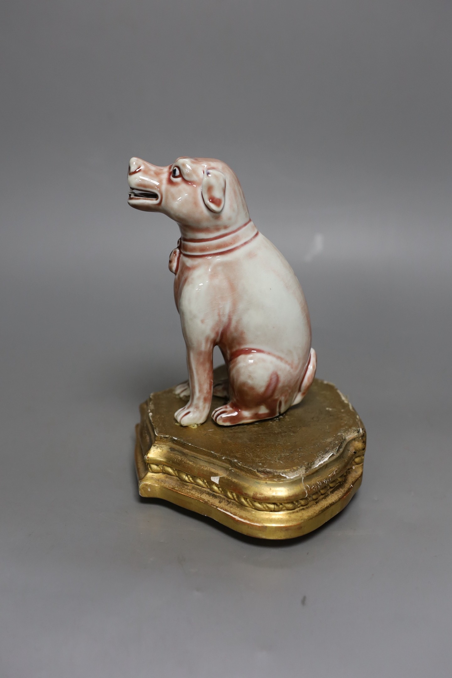 A Chinese porcelain model of a seated dog on gilt wood stand, 19cm tall